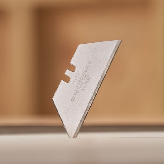 Photo of STANLEY 11-921 utility knife blade, silver color, angled on white surface, close-up.