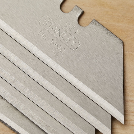 Photo of STANLEY 11-921 utility blades stacked on a wooden surface, showing sharp metal edges.