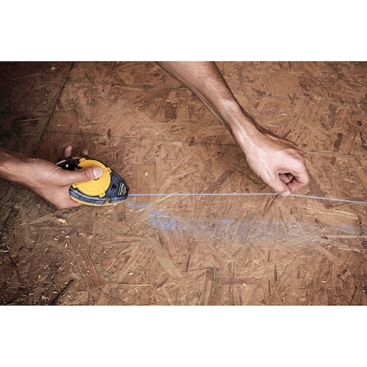 Photo of STANLEY 47-464 chalk line tool marking plywood surface, close-up action angle.