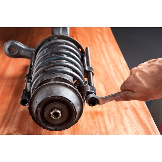 STANLEY spring compressor in use on car strut, SKUs 79-028LA and 79-028, close-up on wood surface.
