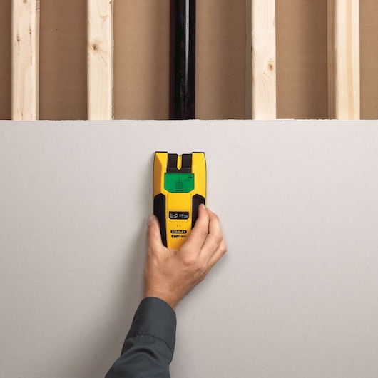 Stanley FMHT77407 stud finder in use on drywall, yellow and black handheld electronic tool.