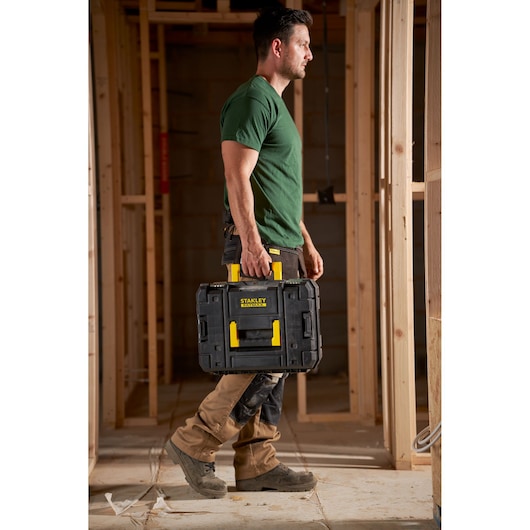 Photo of a person carrying a STANLEY FMST1-71966 black tool box with yellow handle at a construction site.
