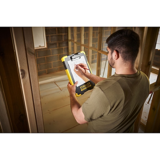 Photo of STANLEY FMST82721-1 clipboard held on construction site, showing yellow and black durable design.