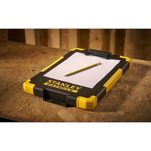 STANLEY FMST82721-1 clipboard with yellow corners, pencil and paper, angled view on wooden table.