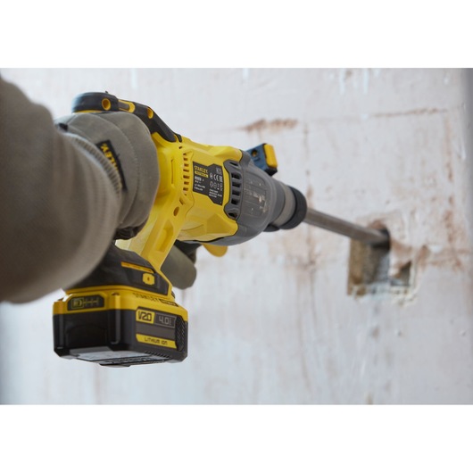 Photo of STANLEY SBH900 rotary hammer drill in use, drilling into a concrete wall, close-up on tool and battery.