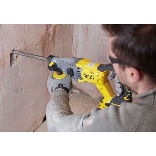 Photo of STANLEY SBH900 rotary hammer in use, yellow and black, drilling into plaster wall, construction setting.