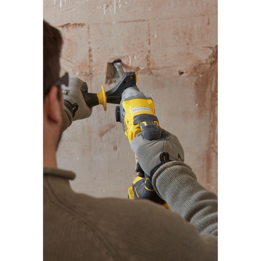 STANLEY SBH900 rotary hammer in use against a plaster wall, rear angle, yellow and black power tool.