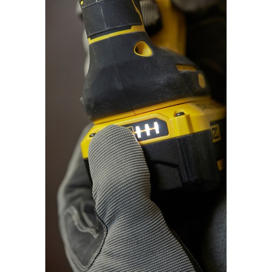 STANLEY SBH900 drill close-up with gloved hand pressing battery indicator, yellow and black, photography