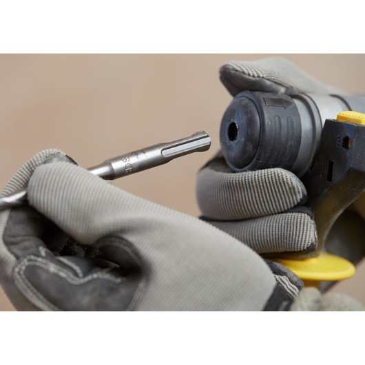 Photo of STANLEY SBH900 rotary hammer being fitted with a drill bit, gloved hands holding the tool close-up.