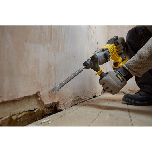 STANLEY SBH900 rotary hammer drill in use chipping plaster from a wall, close-up side view.