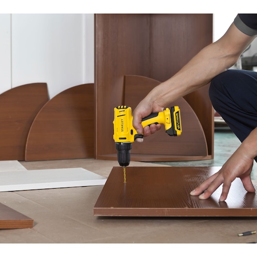 STANLEY SCD121S2K-BR cordless drill in use drilling into wood, close-up of hand holding tool.