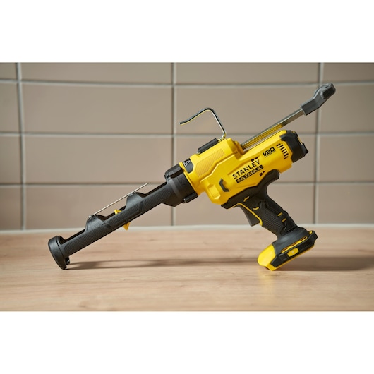 Stanley SCE600B cordless yellow caulking gun on tabletop, side angle view.