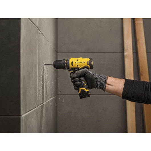 Photo of STANLEY SCH10 cordless drill being used to drill into gray tile wall, close-up action.