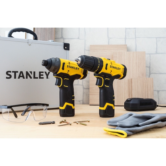 STANLEY SCHI10 cordless drill and impact driver set on table with case, charger, safety glasses, screws, and gloves.