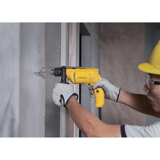 STANLEY SDH600K yellow corded hammer drill used by worker drilling into concrete wall.