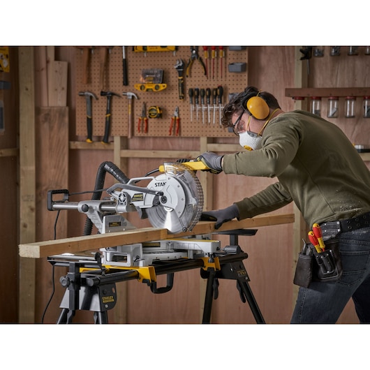 STANLEY SM181 miter saw in use, cutting wood on a STANLEY stand, workshop background, side angle.