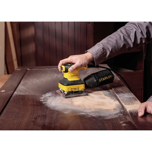 STANLEY SS24-B3 sheet sander being used to sand a wooden surface, close-up with dust collector visible.