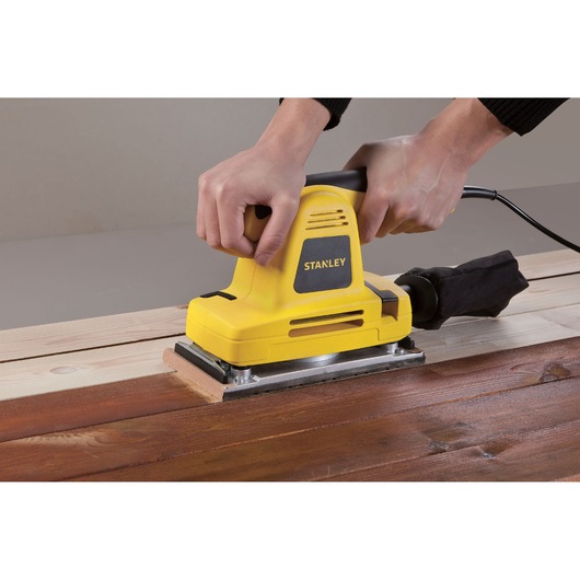 Photo of STANLEY SSS310 yellow sheet sander used on wooden surface, shown from side angle.