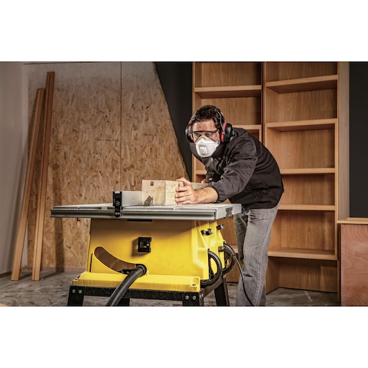 STANLEY SST1801-B3 table saw in workshop, side view, cutting wood with operator wearing hearing protection.
