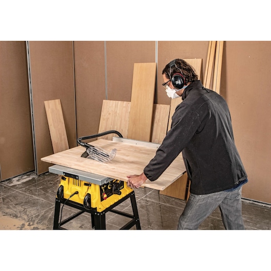 STANLEY SST1801-B3 table saw in use cutting wood panel, person wearing hearing protection, indoor workshop.