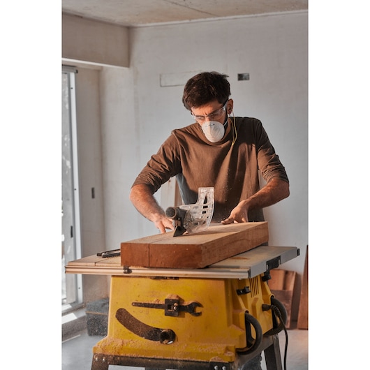 Photo of a person using a STANLEY SST2001-B2 table saw to cut wood indoors, yellow base visible.