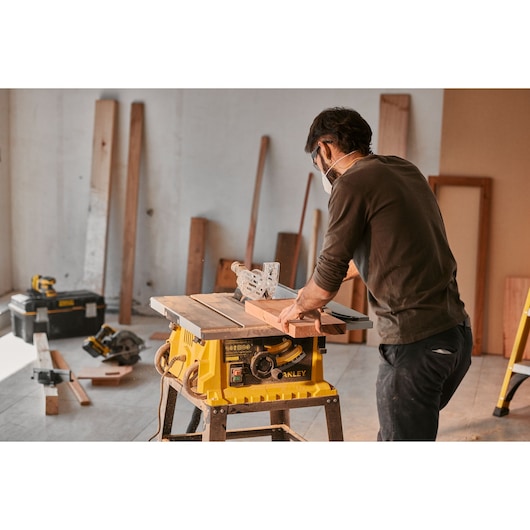 STANLEY SST2001-B2 table saw in use on a workshop floor, person cutting wood with safety equipment.