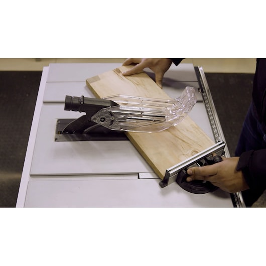 STANLEY SST2001-B2 table saw with clear blade guard, shown cutting a wooden board, top view.