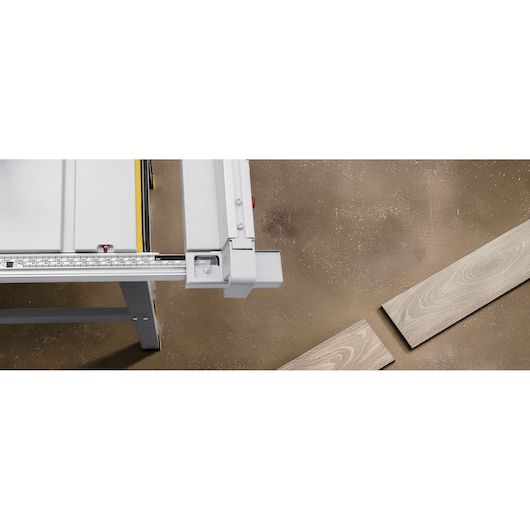 STANLEY SST2001-B2 table saw close-up with metal guide rail and wood planks on brown floor, top view.