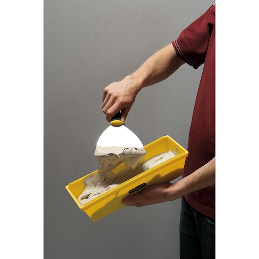 Photo of STANLEY STHT05866LA yellow mud pan filled with joint compound, held with a putty knife.