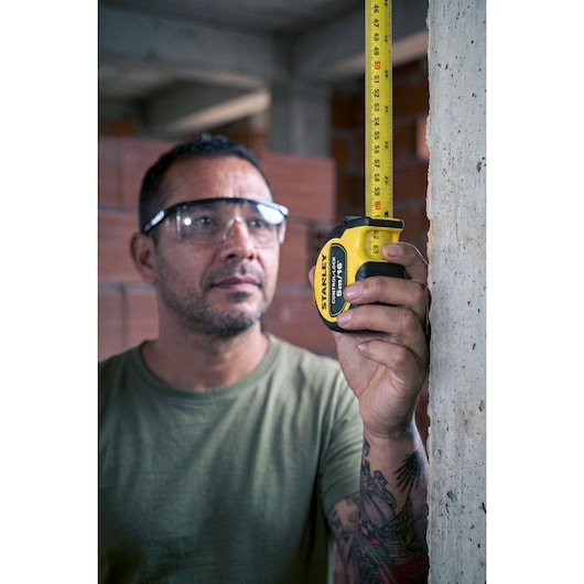Photo of a person measuring a wall with a STANLEY tape measure, SKU STHT37246-0, in a construction setting.