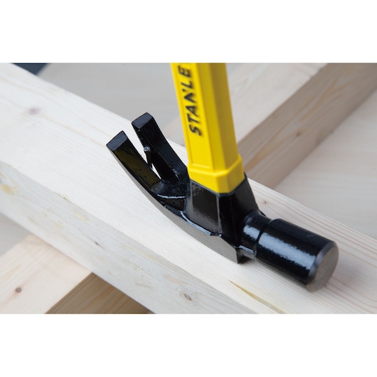 Photo of STANLEY STHT51391 claw hammer with yellow handle in use on wooden beams, angled side view.