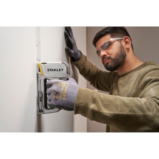 Photo of Stanley STHT70250 heavy duty stapler in use, held by gloved hand against a white wall.