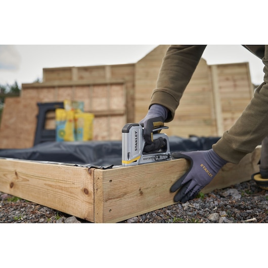 Photo of STANLEY STHT70250 heavy duty stapler being used to fasten material to a wooden frame outdoors.