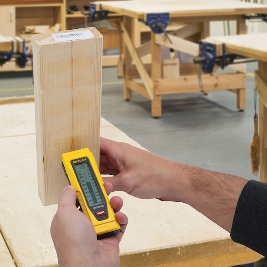 STANLEY STHT77030 moisture meter measuring wood in a workshop, held in hand, close-up view.