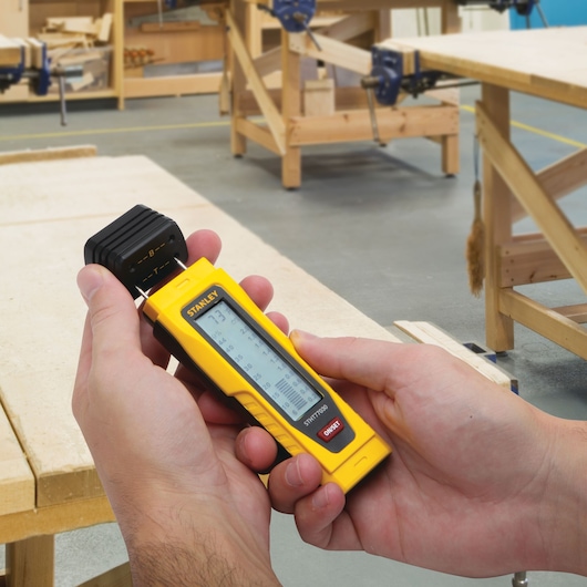 Photo of STANLEY STHT77030 wood moisture meter held in hands in a woodworking workshop.