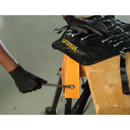 STANLEY STMT25147 wrench in use, black tool roll on wooden workbench, photography from above angle.