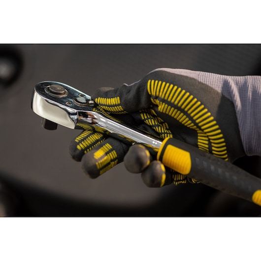 STANLEY STMT82830-LA ratchet held by gloved hand, close-up angle with black and yellow grip detail.