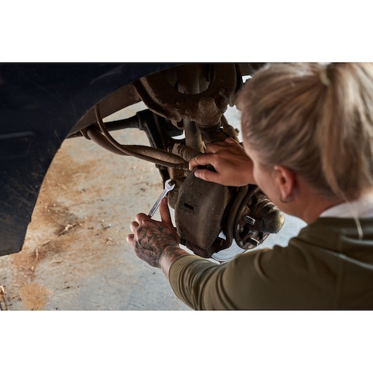 STANLEY STMT82832-LA combination wrench being used to repair a vehicle brake system, close-up view.