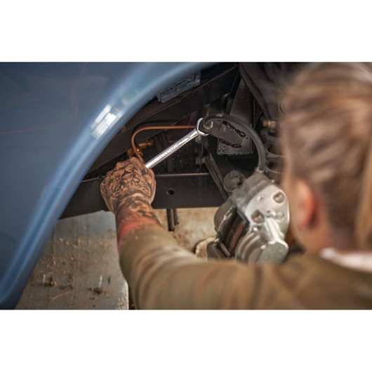 STANLEY STMT82832-LA combination wrench being used to repair a vehicle part in a workshop setting.