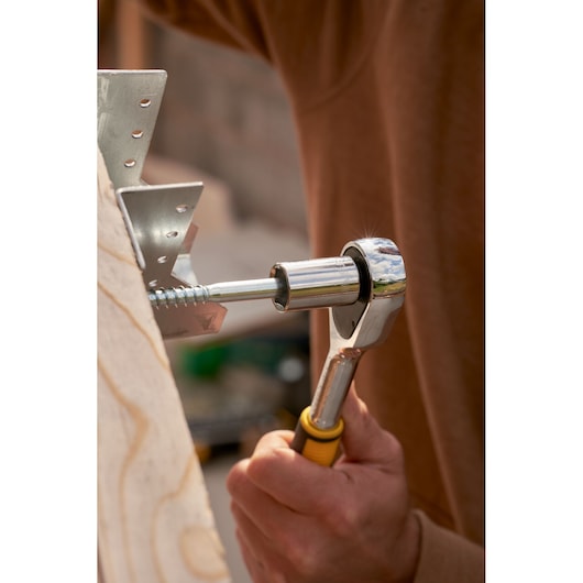 STANLEY STMT82832-LA ratchet wrench in use tightening metal bracket screw, close-up photo.