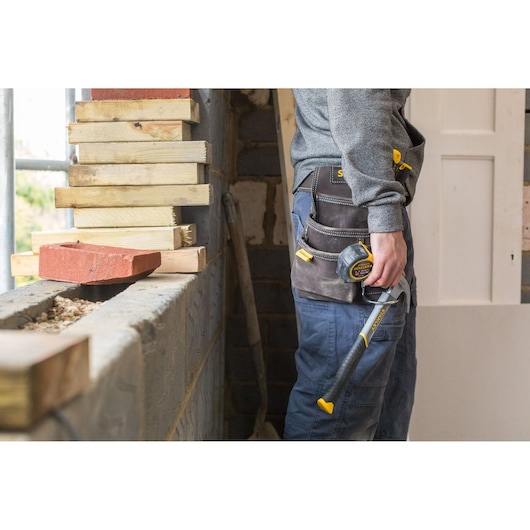STANLEY STST1-80114 tool belt worn by worker, holding hammer and tape measure, construction site setting