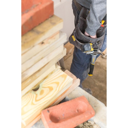 STANLEY STST1-80114 tool belt on person’s waist with hammer, close-up, construction site background.