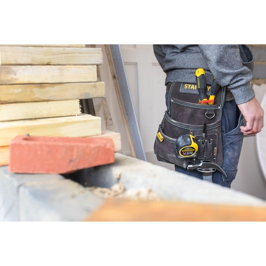Photo of STANLEY STST1-80114 tool belt with yellow tape measure and hand tools worn by a person at a worksite.