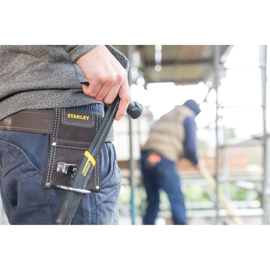 STANLEY STST1-80117 tool belt on worker’s waist with STANLEY hand tool, construction site background.