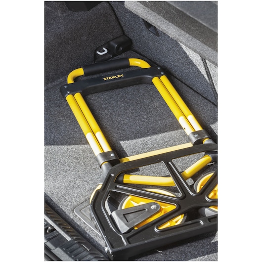Stanley STST98022L folding hand truck with yellow frame, photographed inside a car trunk.