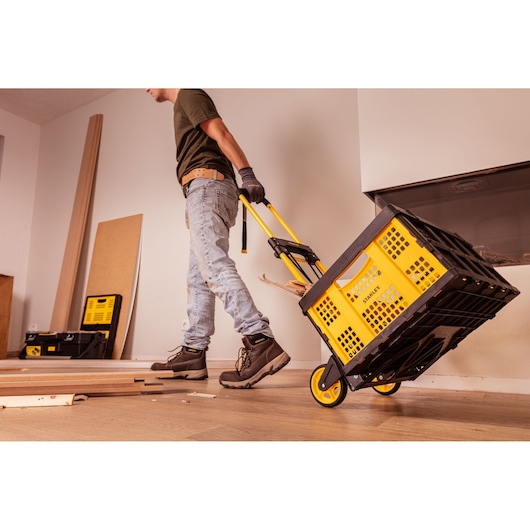 Photo of STANLEY STST98022L yellow folding crate on wheels being pulled by a worker indoors.