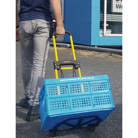 STANLEY STST98022L folding hand truck with yellow handle, blue basket, photographed outdoors in use.