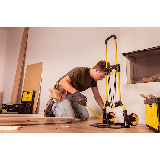 Stanley STST98022L yellow hand truck in use, photographed in a construction setting with tools and materials.