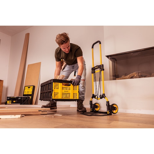 STANLEY STST98022L yellow and black folding hand truck with crate, indoor workspace setting.