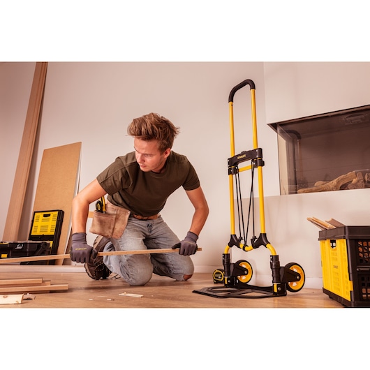 Stanley STST98022L folding hand truck with yellow frame, used by worker in indoor setting.